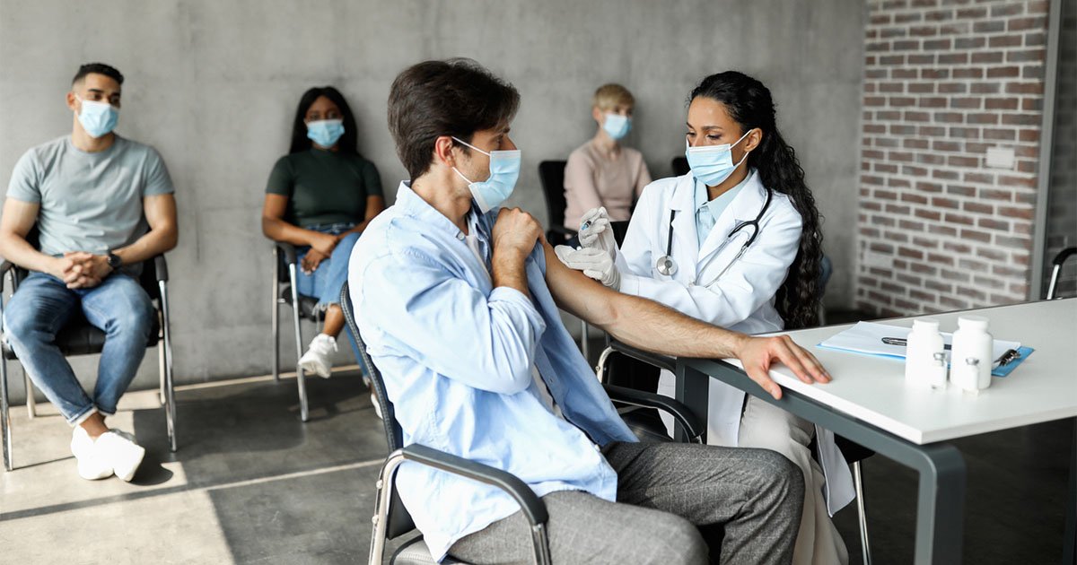 Man getting intramuscular shot against COVID-19 at clinic Masked health worker with a patient, delivering vaccines